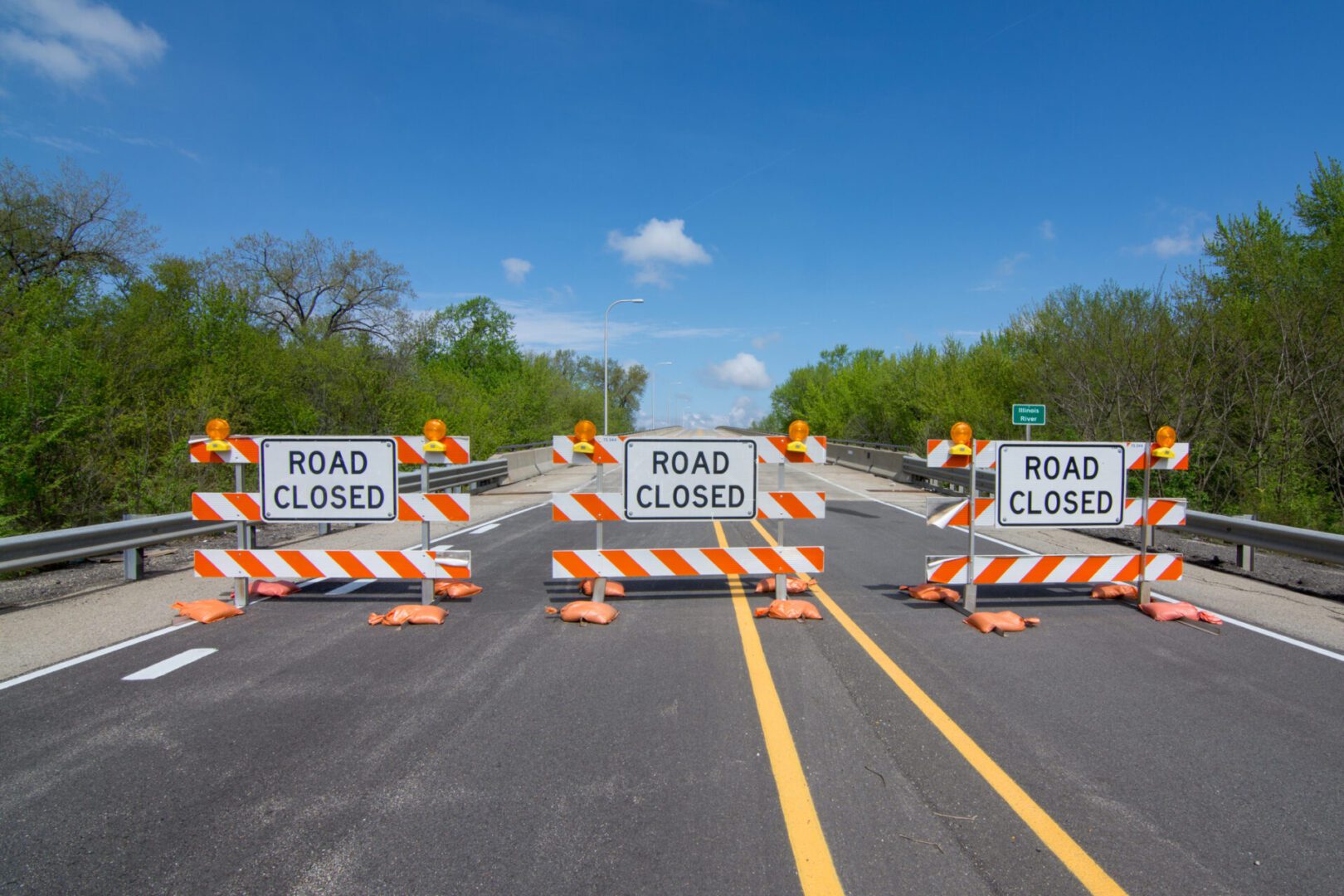 A road closed sign with orange and white cones.